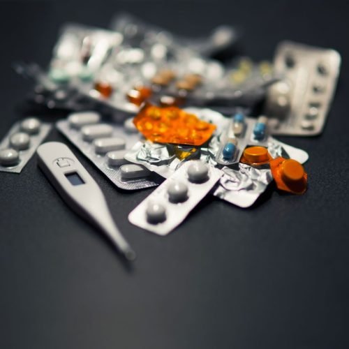 Close-up of various pills and a digital thermometer against a dark background.