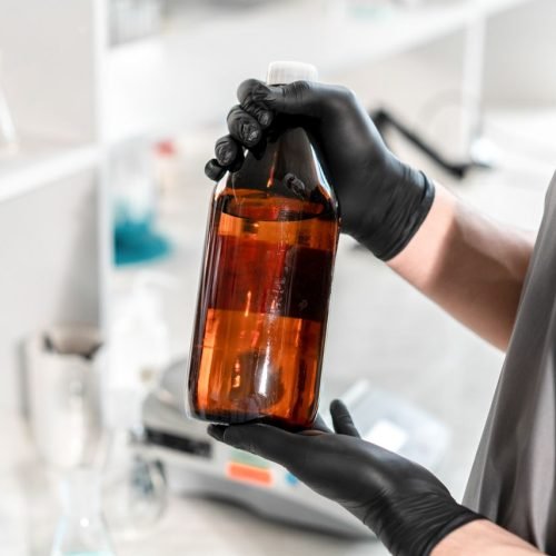Scientist's hands with black gloves holding a brown glass bottle in the laboratory for research.